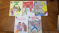 Photo of five Sesame Street hardcover books on a wood floor. Titles visible: Show and Tell, Molly Moves to Sesame Street, Everyone Makes Mistakes, The Case of the Missing Duckie, Special Delivery.
