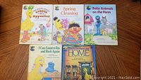 Five Sesame Street hardcover books arranged on a wooden surface with covers facing up showing colorful illustrations of characters including Big Bird, Ernie, and Cookie Monster.