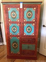 Front view of hand-painted armoire with floral medallion design and lot tag