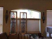 Full view of both metal wall sconces flanking the window blinds and the two large decorative metal and wood wall hangings in front of the window.