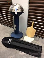 Electric Masterbuilt Veranda grill standing on concrete floor with grill cover, pizza server, and pizza stone beside it.