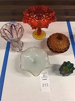 Five vintage glass items displayed on a table: amber carnival glass pedestal bowl, acorn lidded dish, clear cut glass vase, opaque white glass dish, and small green candle holder.