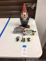 Full view of all items on a white table including Mickey Mouse gnome statue, two picture frames, and six figurines.