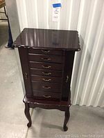 Full front view of the closed jewelry stand highlighting dark wood finish, decorative curved legs, and brass drawer handles