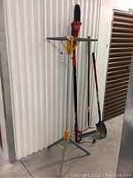 Full view of electric pole chainsaw on stand with shovel and rake behind