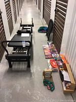 Wide angle photo showing Aero Pilates reformer machine, DVDs, resistance bands, and other fitness accessories laid on the floor of storage hallway.