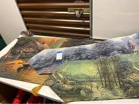 Three Thomas Kinkade woven tapestries arranged folded on a table, showing mixed autumn and evening light themed pastoral scenes with houses, trees, and bridge.