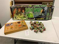 Photo showing the Green Ghost game box featuring artwork of people playing the game and the translucent green ghost game piece, along with the wooden block puzzle showing several blocks with illustrations and text.