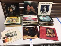 Photo showing multiple stacks of vintage vinyl records on a table, featuring John Lennon and Yoko Ono, Steve Miller Band, Herschel Bernardi, and Barbara Streisand albums prominently displayed.