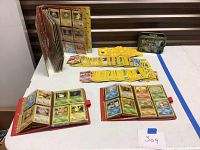 All three binder albums, loose cards spread on table, Pokemon tin at rear