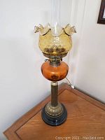 Full view of vintage banquet lamp showing amber glass components, brass column, and black base from front angle.