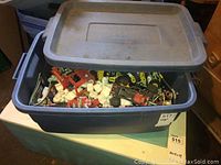Large gray plastic storage bin partially open showing assorted Lego Technic parts inside with white packing foam