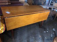Full view of the wooden drop leaf table with leaves closed, showing wood finish and four legs.