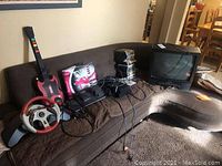 Overview of all electronics on couch: TV, PS2 console, controllers, games, accessories