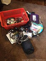 Overview of assorted electronic items including a red basket holding various gadgets and tangled electronic cords on the floor.