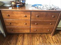 Front view of medium brown wooden dresser with six drawers and some scratches. One drawer is missing a pull.