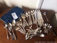 Full view of Community Plate cutlery laid out on table including forks, knives, spoons, and teaspoons with a blue cloth pouch.