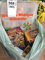 Photo showing Yu Gi Oh! trading card binders and two metal storage boxes inside a plastic bag, with Western Michigan University branding on binder.