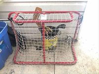 Red mini hockey net indoors on concrete floor with hockey sticks inside bucket.