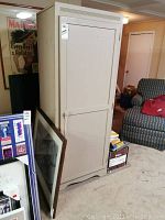 Full stand view of the beige single door cabinet with rod inside, showing front and partial side view along with surrounding living room content for scale.