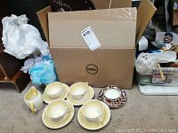 Four yellow and white porcelain teacups and saucers with one Royal Crown Derby teacup and saucer in front of a cardboard box.