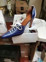 Single blue and white leather bowling heel shoe with lace-up front on a brown sole, placed on top of a white box.