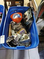 Full view of blue bin containing various plastic dishware, plastic containers, cups, and a bag.