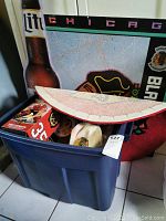 Blue plastic tote with red Chicago Blackhawks round accent rug on top, tin wall sign and various items visible inside