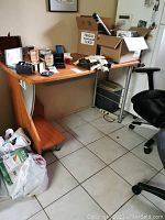 Desk with wooden top, curved wooden support on one side with shelving, and metal leg support on other side. The desk surface has multiple items on it, not included in sale.