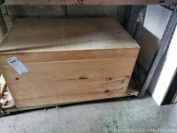 Small wooden chest on metal shelving unit, closed lid, visible wood grain and knots