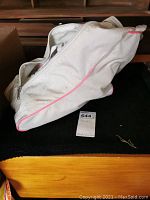 White fabric carry bag with pink piping lying on a surface, zippered closed