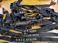 Photo showing multiple black cloth naval cap tallies with gold/white embroidered names such as H.M.C.S. Fundy, H.M.C.S. Avalon, Koninklijke Marine, Armada de Chile, etc.