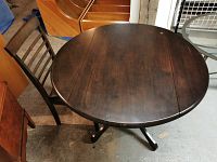 Dark-stained pine round dropleaf table seen from above showing wear and age marks on the surface with one dropleaf folded down.
