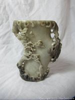 Front view of the carved vase showing the openwork and natural scenery design in stone with dark accent colors near the base.