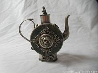 Full front view of round teapot showing spout, handle, and decorative medallion