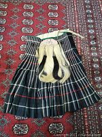 Full view of green and black tartan kilt with attached horsehair sporran laid flat