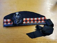 Full side view of navy blue wool Glengarry cap, showing diced band and trailing ribbons