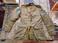 Full front view of khaki wool tunic laid flat showing pockets, ribbon bar and overall condition.
