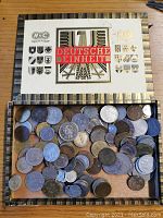 Top view of a vintage box with assorted coins inside shows label 'Deutsche Einheit' and various heraldic crests
