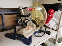 Full side view of Ryobi TS1342L compound miter saw showing saw blade with yellow blade guard, metal base, and fabric dust bag.