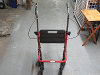 Front view of red folding walker with black seat and handles in a warehouse setting.