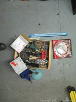 Overhead view of wooden box filled with assorted vintage hand tools and clamps, including metal and wooden handled items, next to a boxed coiled stainless steel item and a blue level bar.