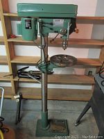 Full view of the green floor-standing drill press showing base, column, table and head assembly