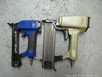 Two pneumatic staple guns on concrete floor showing both items side by side