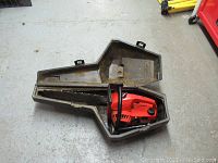 Chainsaw placed inside open carrying case on floor.