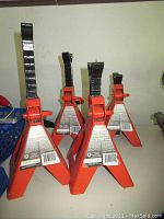 Four orange Motorcraft axle stands with black adjustable arms. The stands display labels and are positioned upright on a flat surface.