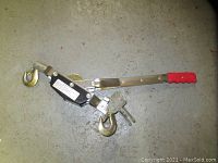 Full view of the portable tow winch showing the red handle, steel frame, and metal hooks on a concrete floor.