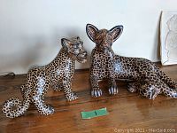 Front view of two handcrafted ceramic jaguar sculptures showing detailed spotted patterns and artist signatures.