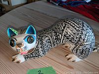 Side view of the Alebrije cat figurine showing the black and white painted geometric patterns and blue accents on the face and ears.