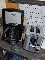 Photo showing Delonghi drip coffee maker next to Black & Decker stainless steel 2-slot toaster on a table